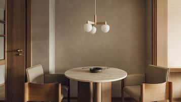 A modern dining area with a round table, two wooden chairs, and a minimalist pendant light.