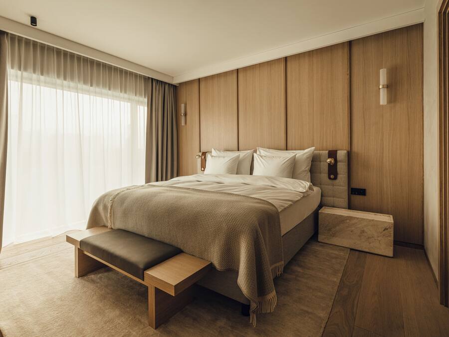 Een moderne slaapkamer met een groot bed, een bankje en een houten hoofdeinde.