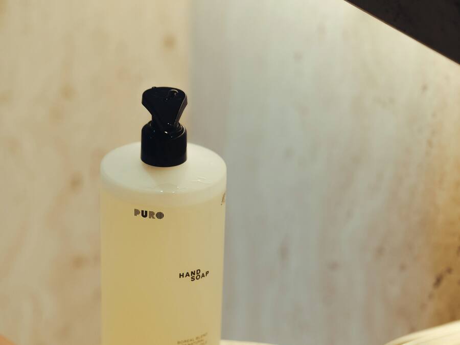 A hand under a running faucet with a bottle of hand soap labeled "PURE HAND SOAP" on the counter.