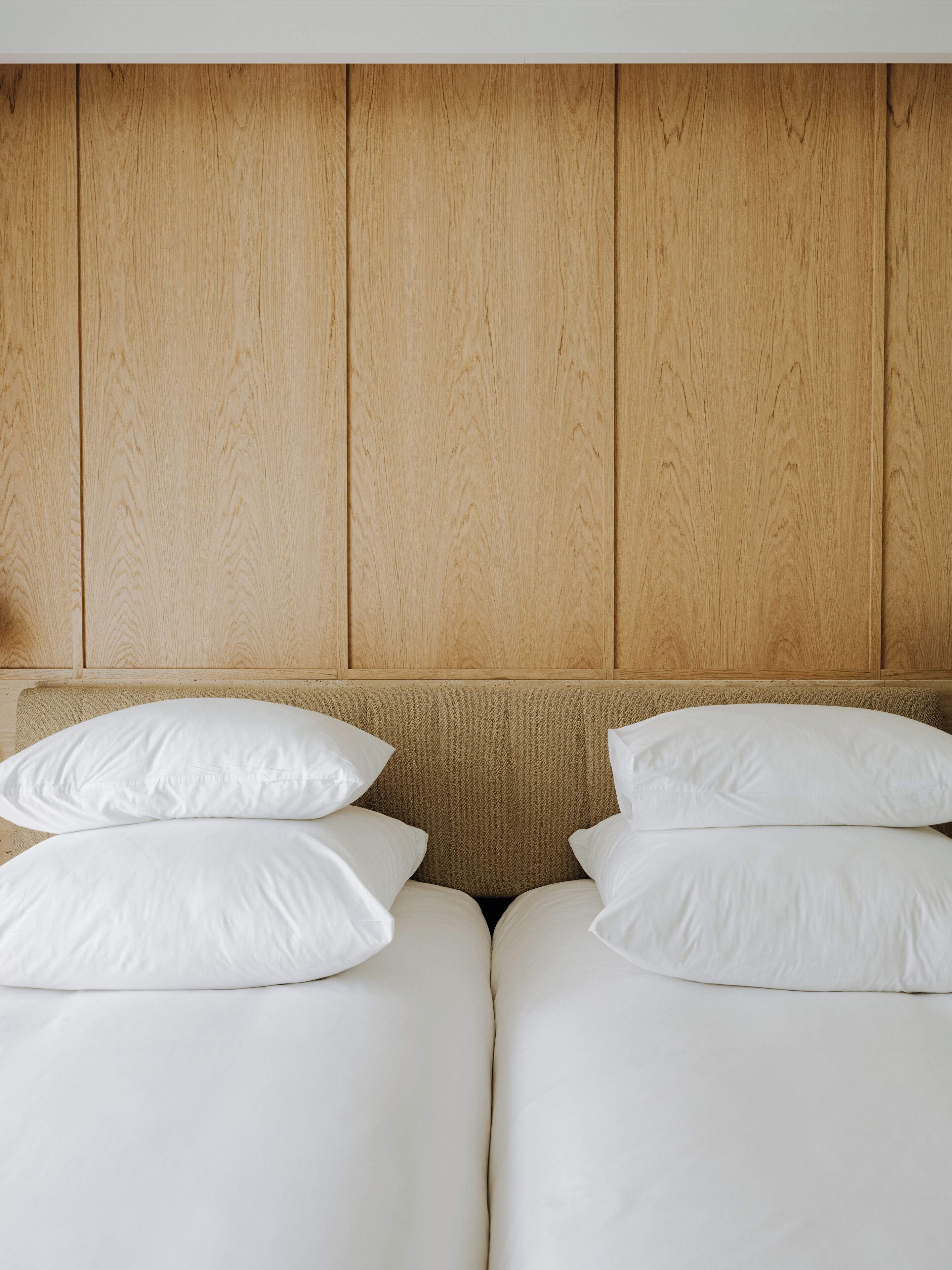 Un dormitorio con cabecera de madera y dos camas con ropa blanca.