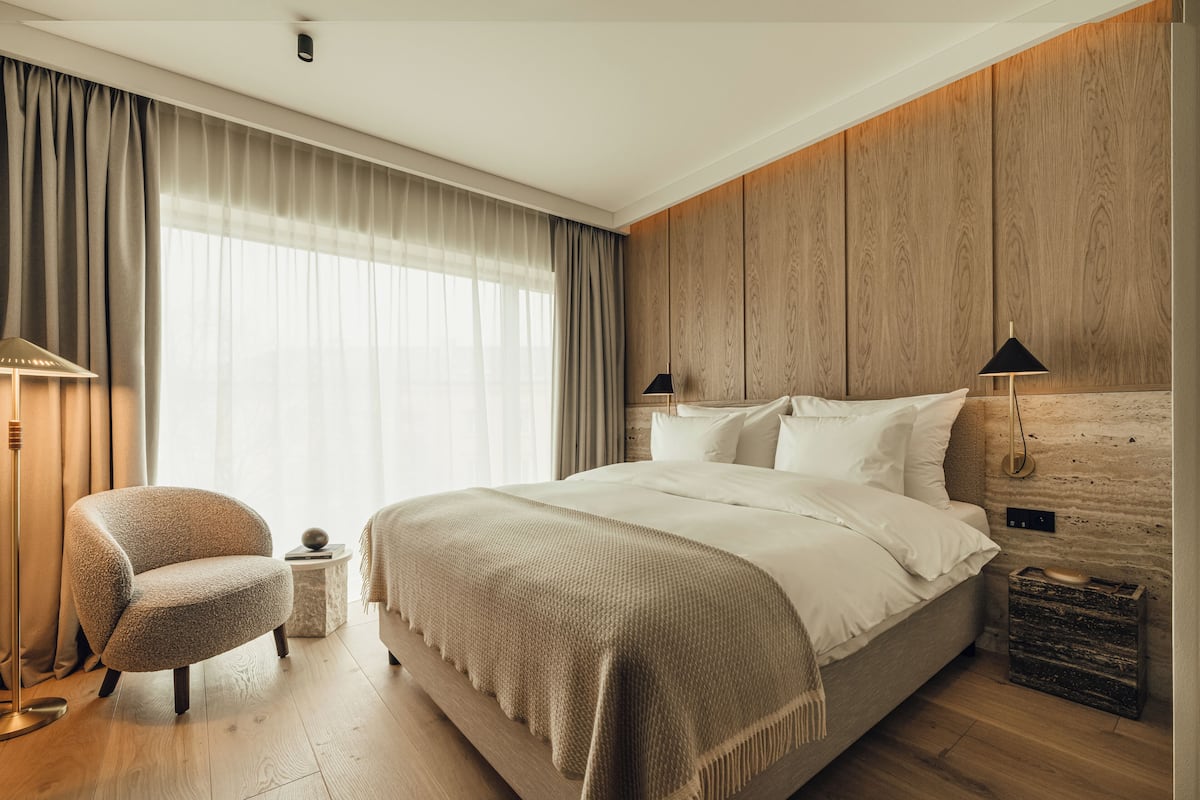 Ein modernes Schlafzimmer mit einem großen Bett, einem Sessel, einem Nachttisch und einer Wand mit Holzpaneelen.