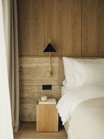 A neatly arranged bedroom with a wooden headboard, a bedside table with a lamp, and a bed with white bedding.
