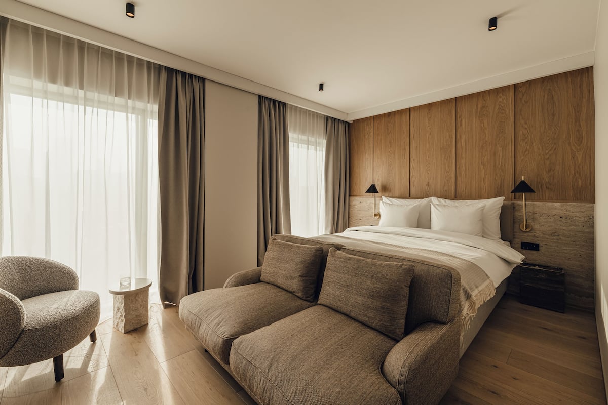 Ein modernes Hotelzimmer mit einem großen Bett, einer Couch, einem kleinen Beistelltisch und einem Sessel.