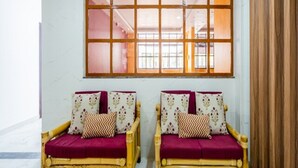 Deux canapés en osier, dotés de coussins rouges et d’oreillers à motifs, sont placés devant une grande fenêtre donnant sur un espace intérieur.