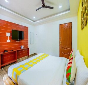 A bedroom with a bed, a television on the wall, a wooden door, and a ceiling fan. - signature grande (Vanur)