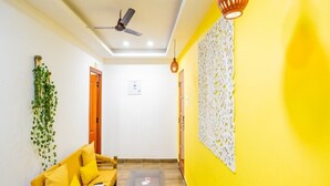 Une pièce avec un mur jaune, un ventilateur de plafond, un canapé avec des coussins, une petite table et un élément décoratif mural.