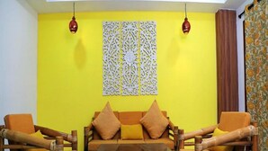 Un salon avec un mur jaune, un panneau décoratif blanc et une table basse en osier marron.