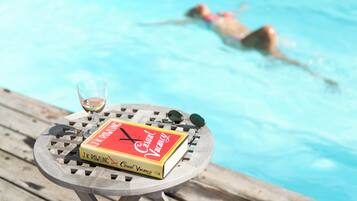 Ein Buch mit dem Titel 'A Casual Vacancy' auf einem runden Holztisch neben einem Pool.