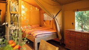 A cozy bedroom with a wooden bed, a dresser, and a window with a view of trees. - Safari tent with all comforts, garden, swimming pool, between La Rochelle and Venise verte (Le Gué-d'Alleré)