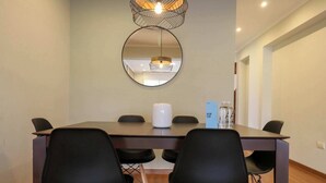 Une salle de conférence avec une table ronde, des chaises noires, un vase blanc et un miroir au mur.