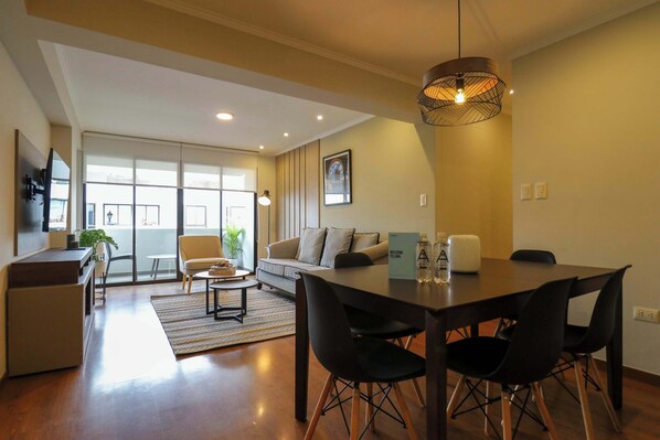 A modern living room with a dining area, a sofa, a coffee table, and a large window providing natural light. - w * | Magnificent 3BR in the Heart of Barranco (Barranco)