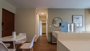 A hotel room with a dining area featuring a white table and chairs, a small kitchen area, a round mirror, and a welcome sign. - w* | Glorious 2BR w/ Perfect Balcony Near Kennedy Park (Miraflores)