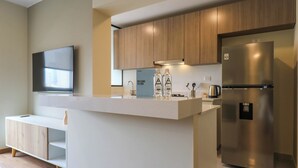 A modern kitchen with wooden cabinets, a stainless steel refrigerator, and a flat-screen TV mounted on the wall. - w* | Glorious 2BR w/ Perfect Balcony Near Kennedy Park (Miraflores)