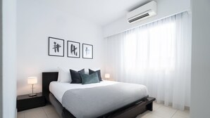 Een moderne hotelkamer met een groot bed, twee nachtkastjes met lampen, een wandairconditioner en drie ingelijste kunstwerken.