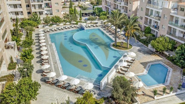 Een resort met een centraal gelegen zwembad, meerdere loungeplekken met parasols en omliggend groen.