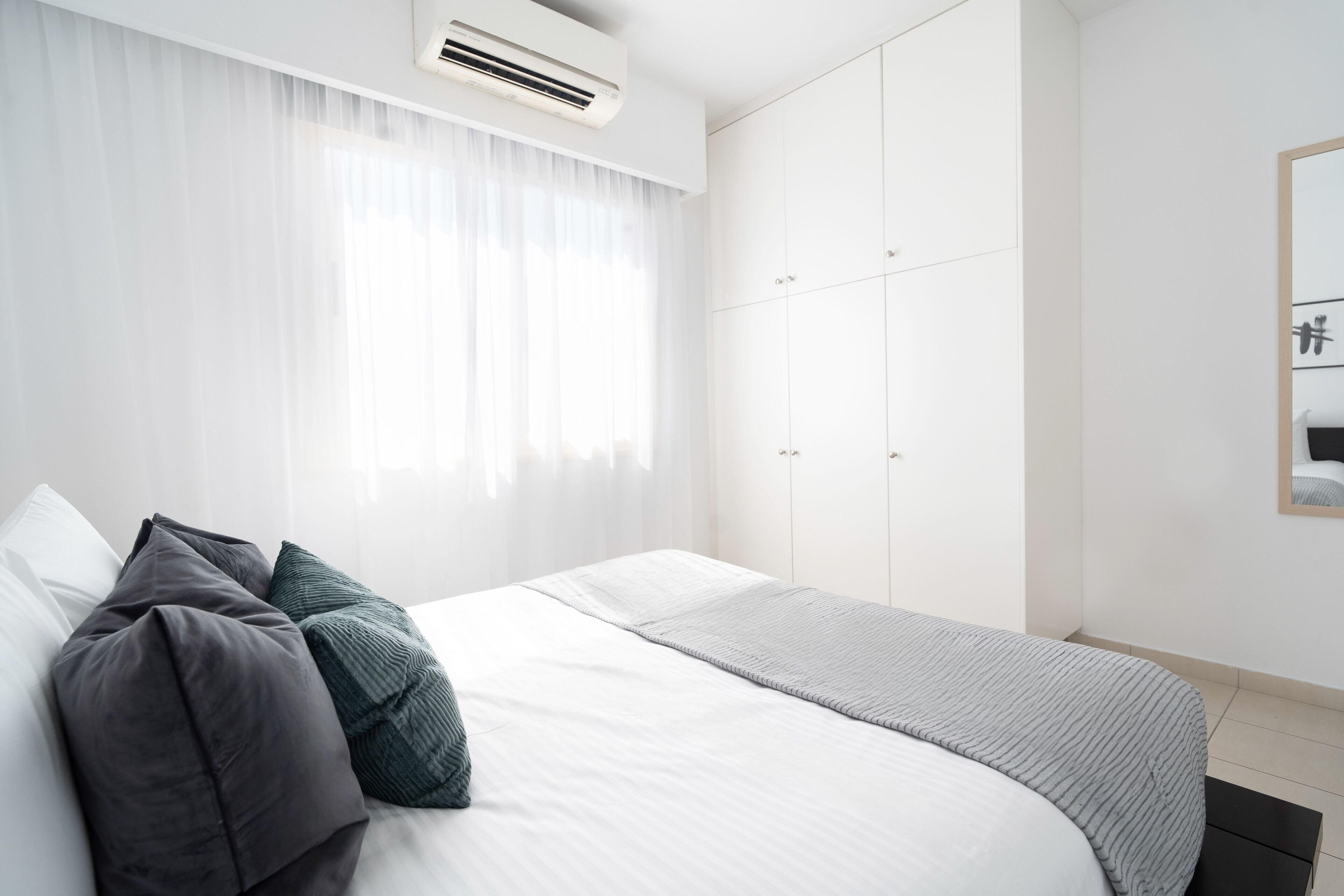 A modern bedroom with a large bed, white curtains, a grey blanket, and a wardrobe with multiple doors.