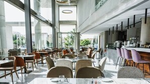 Een modern restaurant met marmeren tafels en stoelen, grote ramen en een bar.