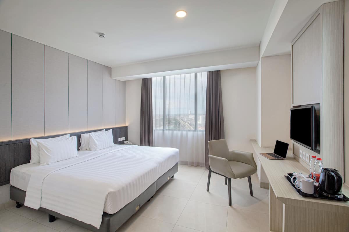 Una habitación de hotel moderna con una cama grande, un escritorio con una computadora portátil, una silla, un televisor y una cafetera.