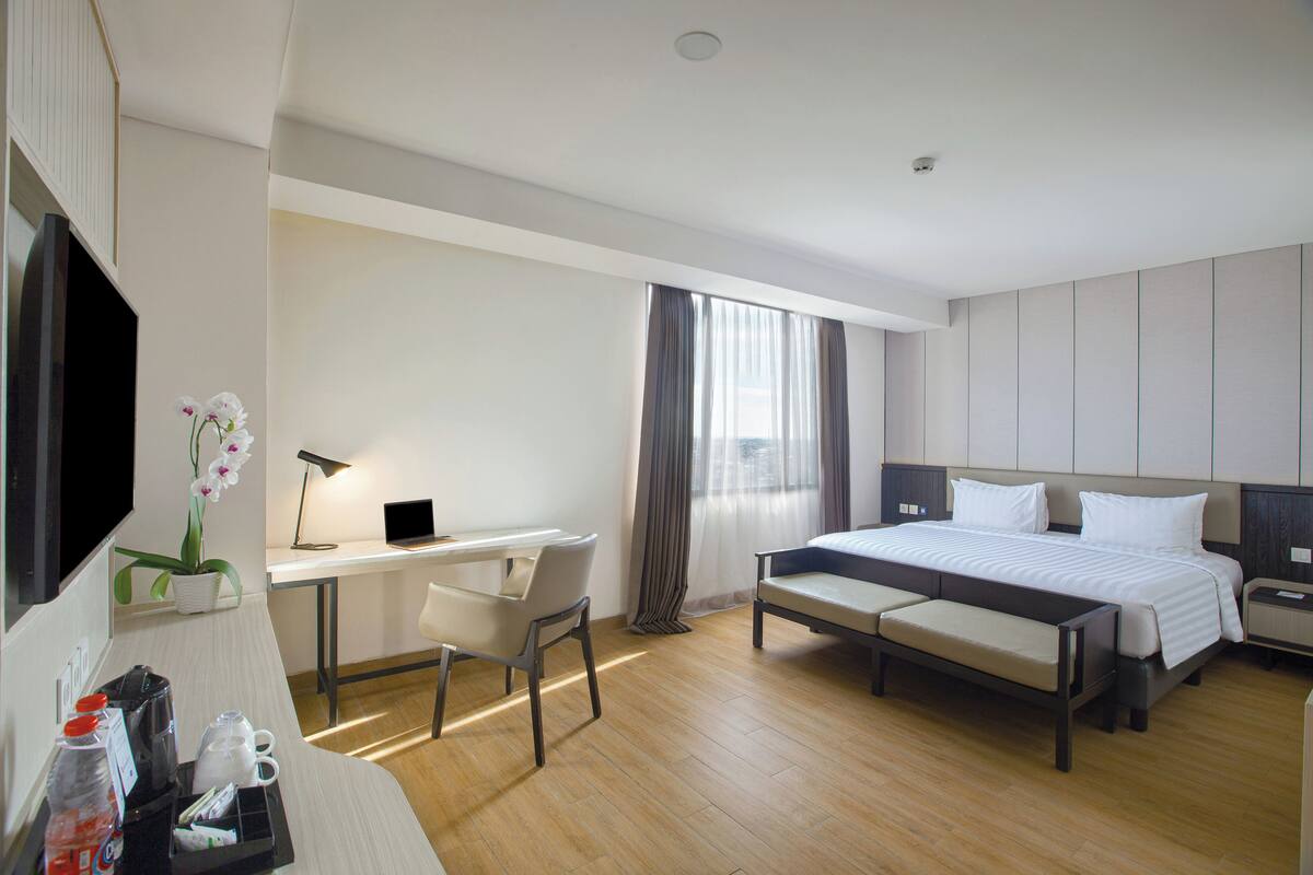 Habitación de hotel con cama, escritorio, silla y una mesita de noche con lámpara.