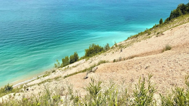 Eine Küstenlandschaft mit freiem Blick auf das Meer, sandigem Gelände und spärlicher Vegetation.