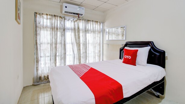 Una camera d'albergo con un letto, una finestra con tende, un condizionatore d'aria e uno specchio fissato al muro.