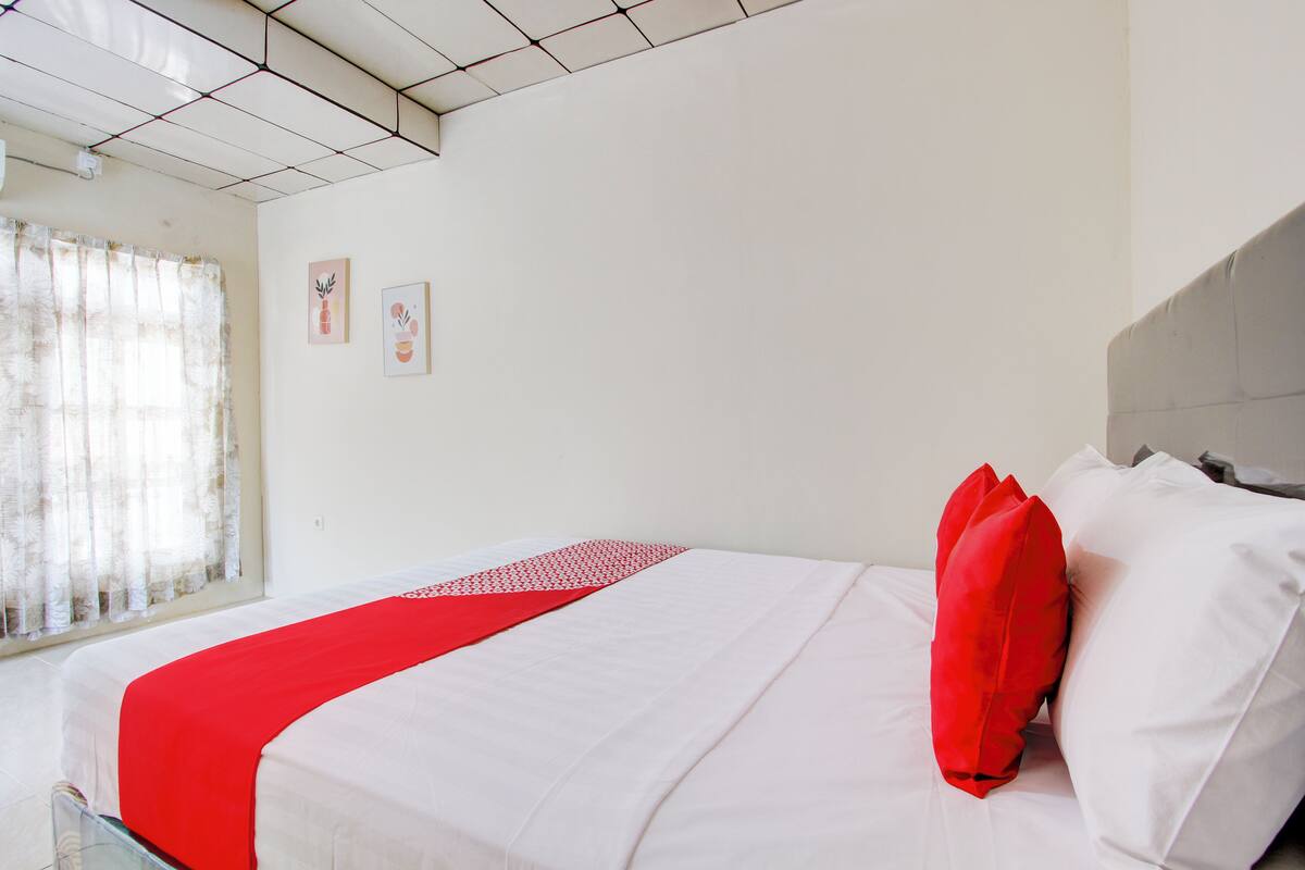 Une chambre d’hôtel avec un lit, une fenêtre avec des rideaux et deux œuvres d’art murales.