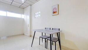 Un'ampia stanza con pavimento piastrellato, una porta bianca, una finestra e un tavolo con sedie.