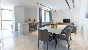 Ein moderner Essbereich mit großem Tisch und Stühlen, einer Küchenzeile und einer Sitzecke mit Sofa und Fernseher.