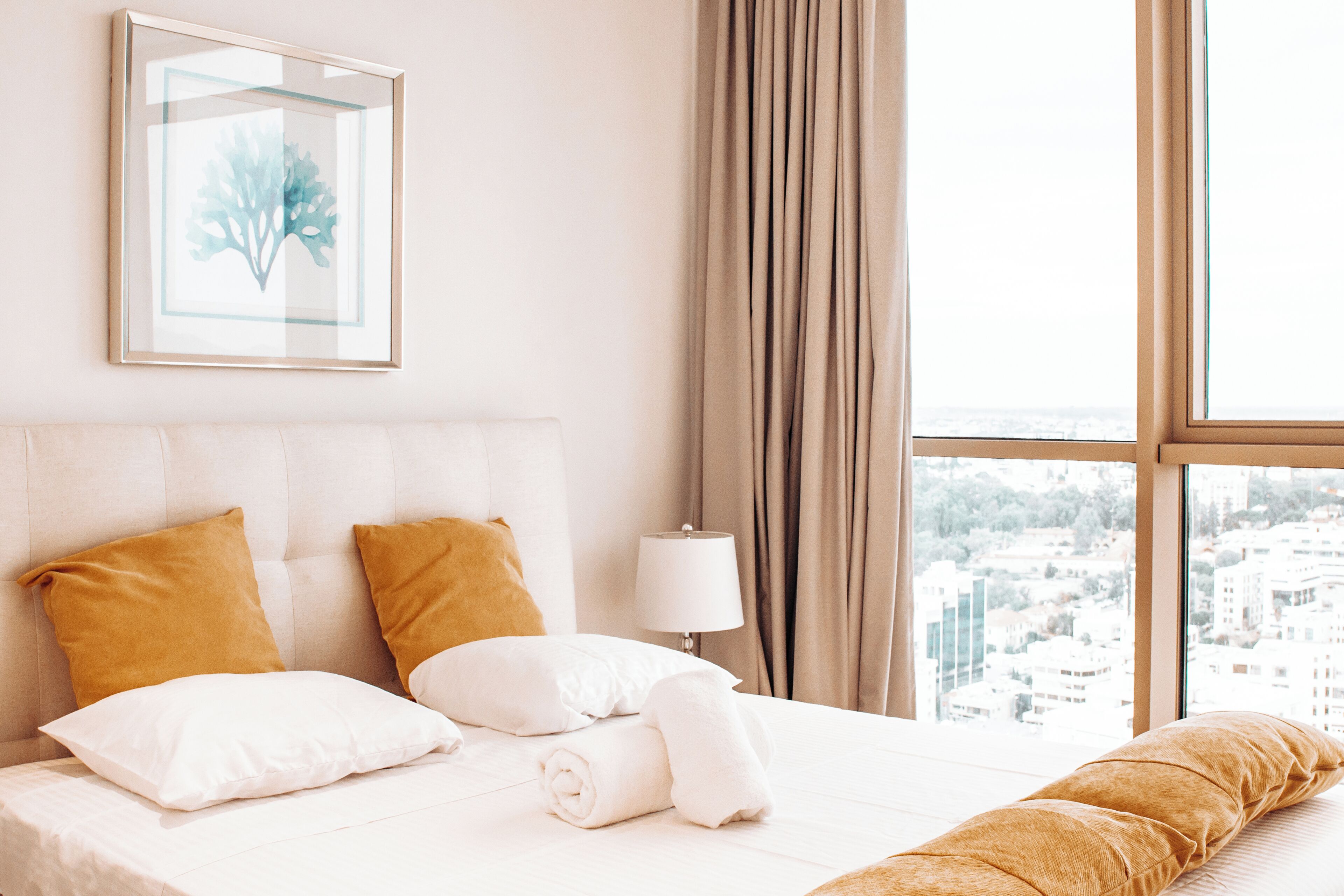 A hotel room with a large bed, two pillows, a rolled towel, a nightstand with a lamp, and a framed picture on the wall.