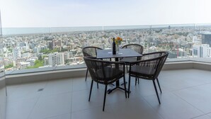 Ein hoher Balkon mit Blick auf die Stadt, ausgestattet mit einem runden Tisch, Stühlen und einem Blumenstrauß.