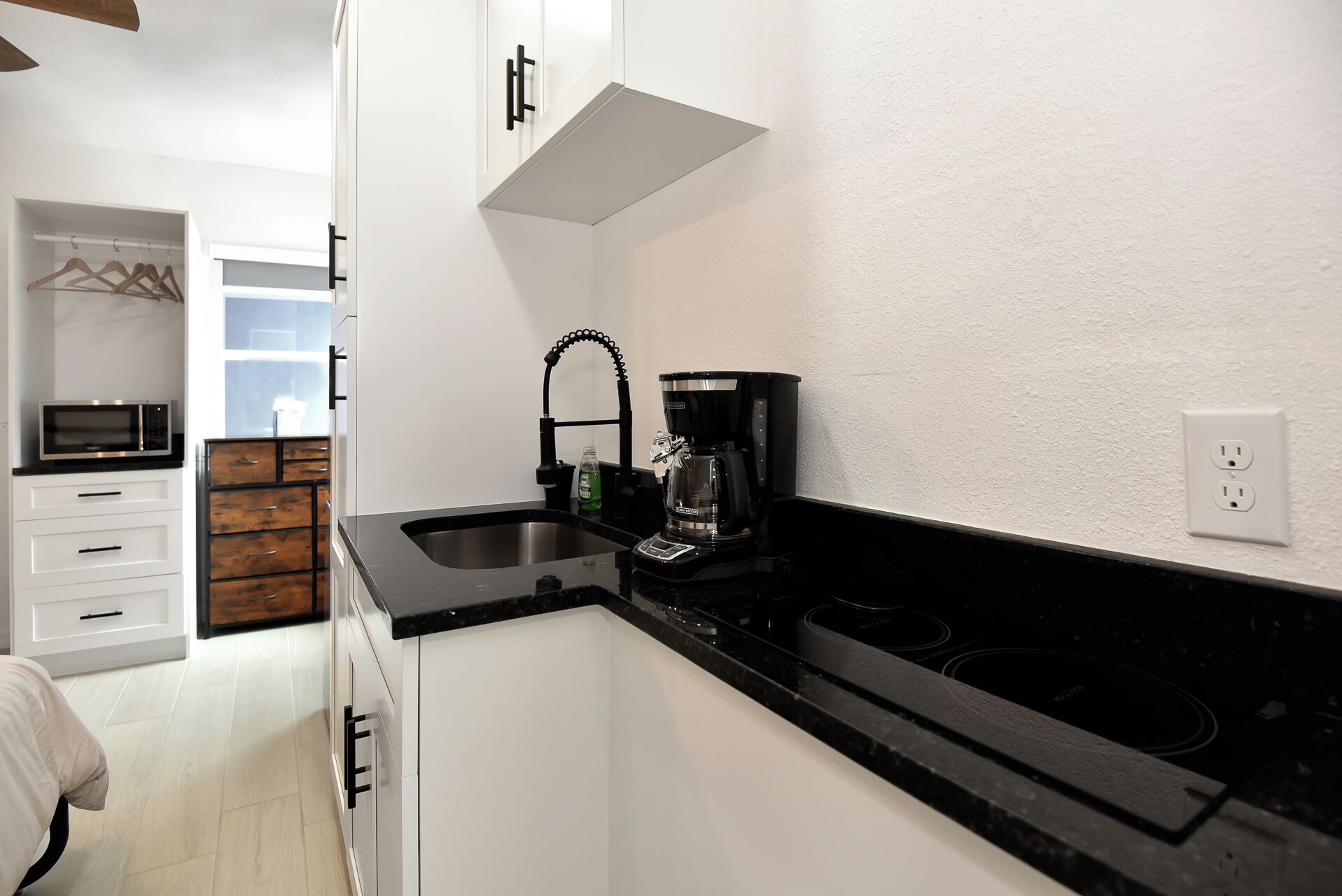 A compact kitchen with white cabinets, a black countertop, a coffee maker, and a microwave.