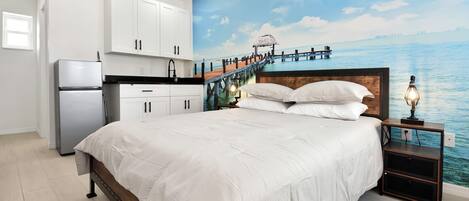 Un dormitorio con cama, mesita de noche y un mural que muestra un muelle que se adentra en el agua.
