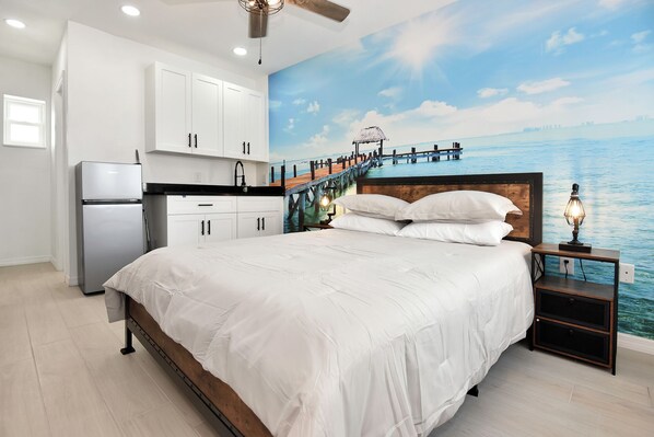 A bedroom with a bed, nightstand, and a mural of a pier extending into a body of water.