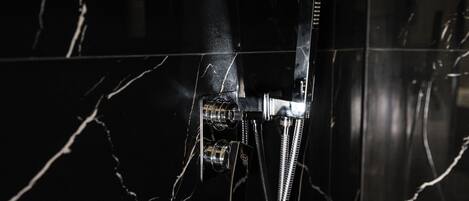 Une douche dotée d’un robinet chromé et d’un flexible, installée sur un mur de marbre foncé aux veines blanches.