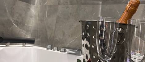 A bathtub with champagne and wine glasses, roses, and a decorative bucket.