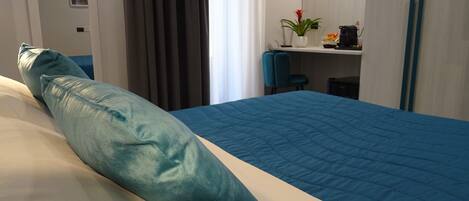 Una habitación de hotel con una cama, un escritorio, una silla, una planta y una estantería con objetos.