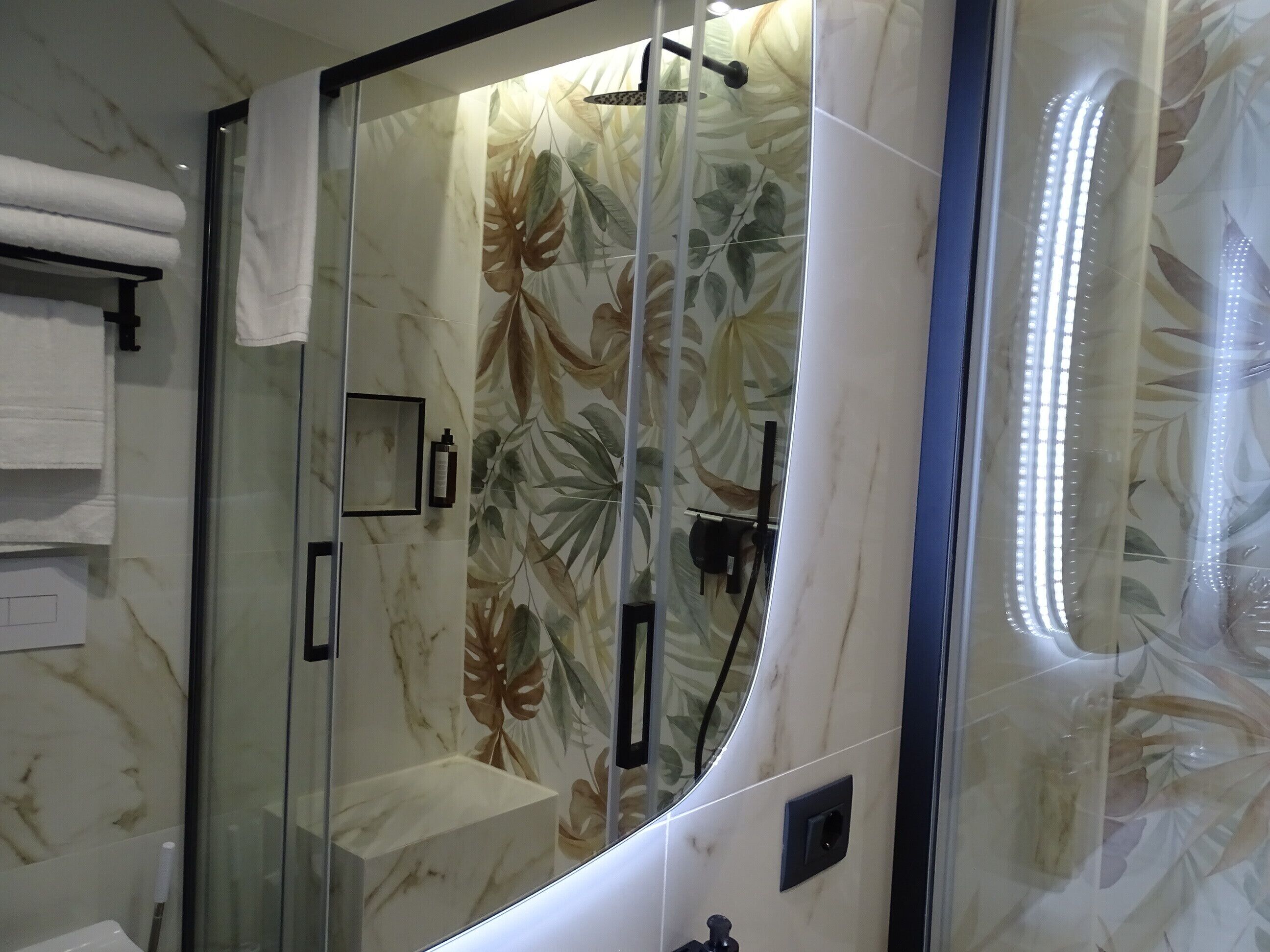 A bathroom with a glass-enclosed shower, marble walls, and a showerhead.