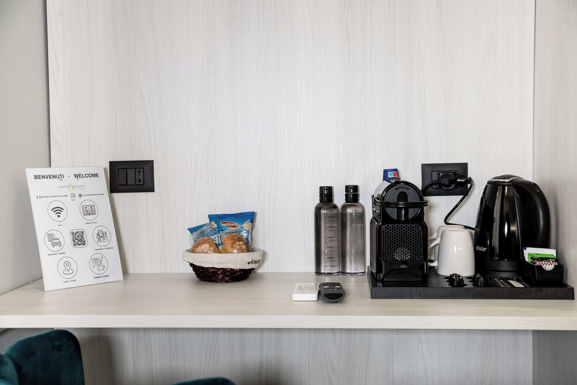 A hotel reception desk with a welcome sign, a basket of snacks, a coffee machine, a kettle, and a water dispenser.