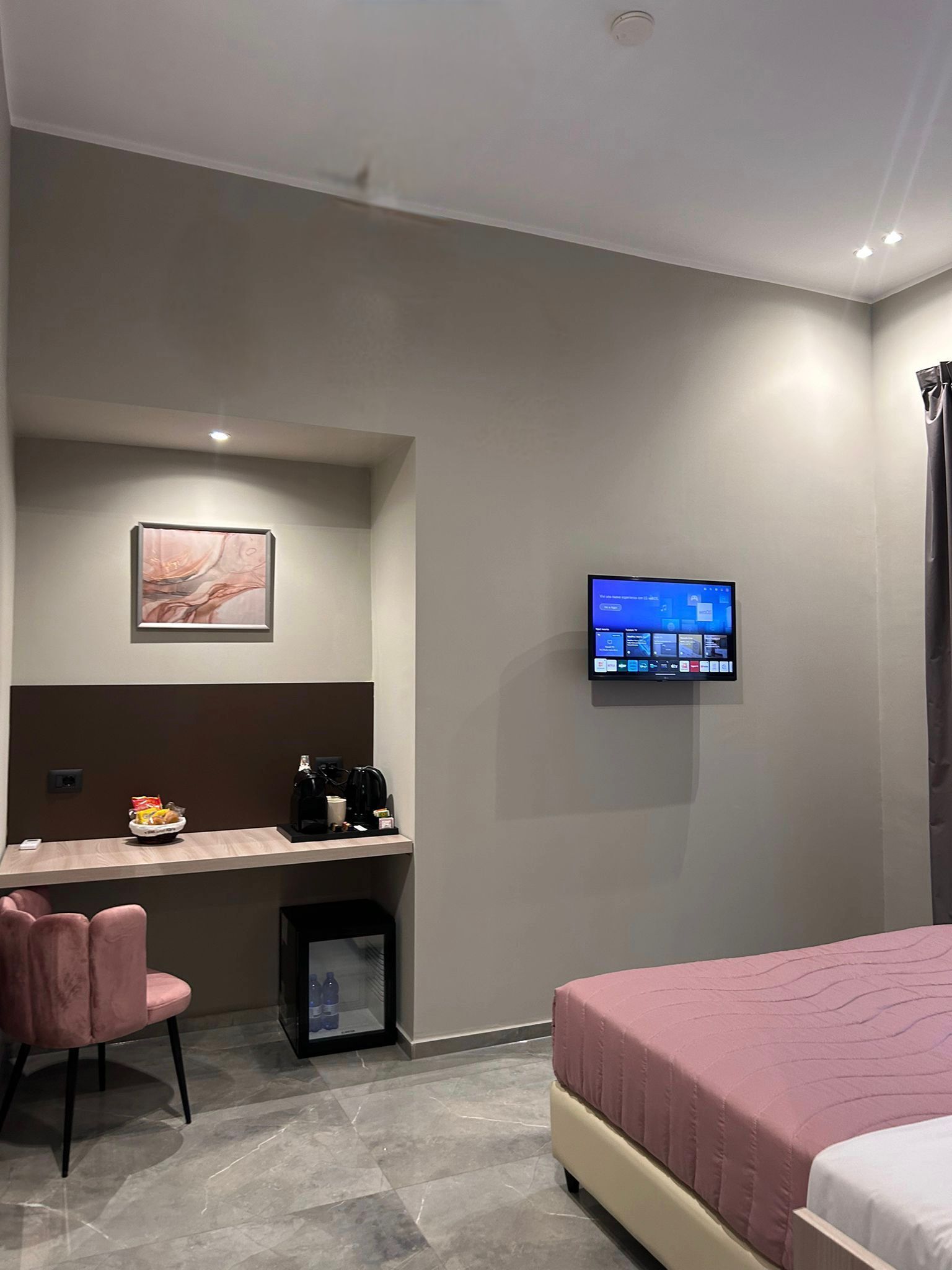 A modern hotel room with a desk, chair, bed, television, and a small trash bin.