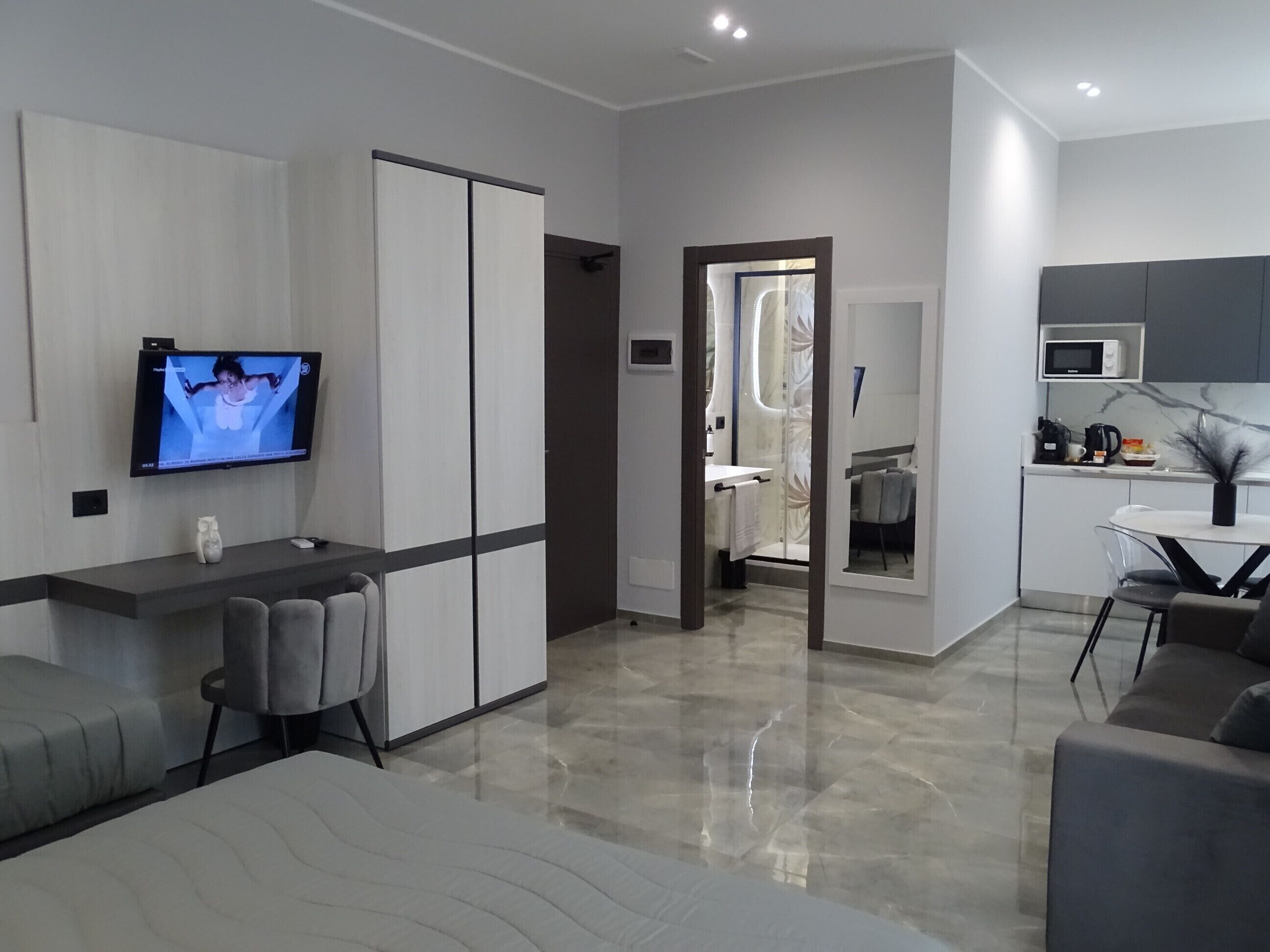 A modern living room with a flat-screen TV, grey sofa, and a dining area with a table and chairs.