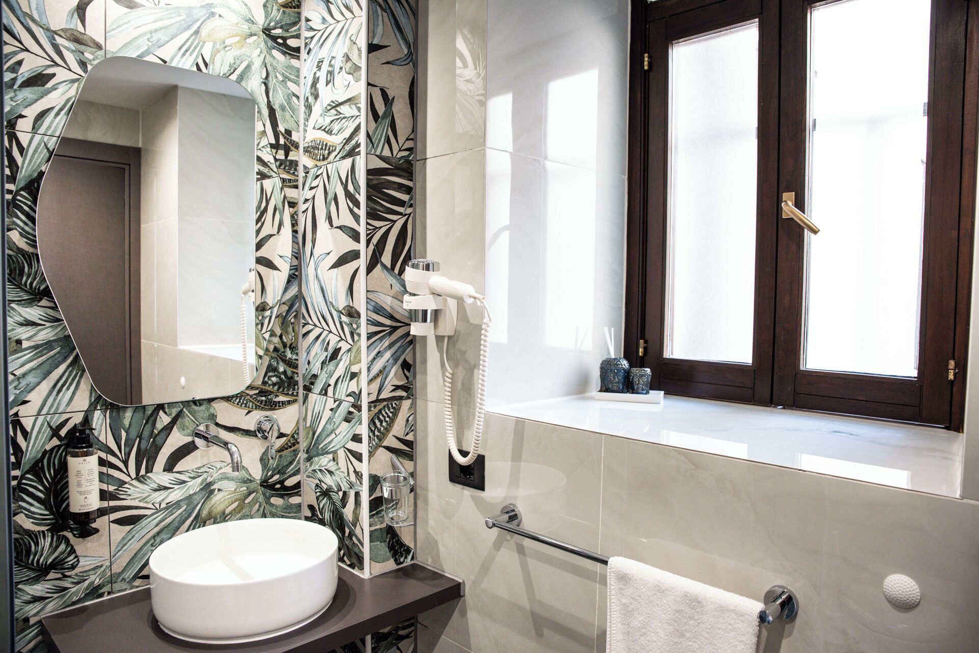 Une salle de bain avec un lavabo blanc, un miroir, un espace douche et une fenêtre donnant sur un beau paysage.