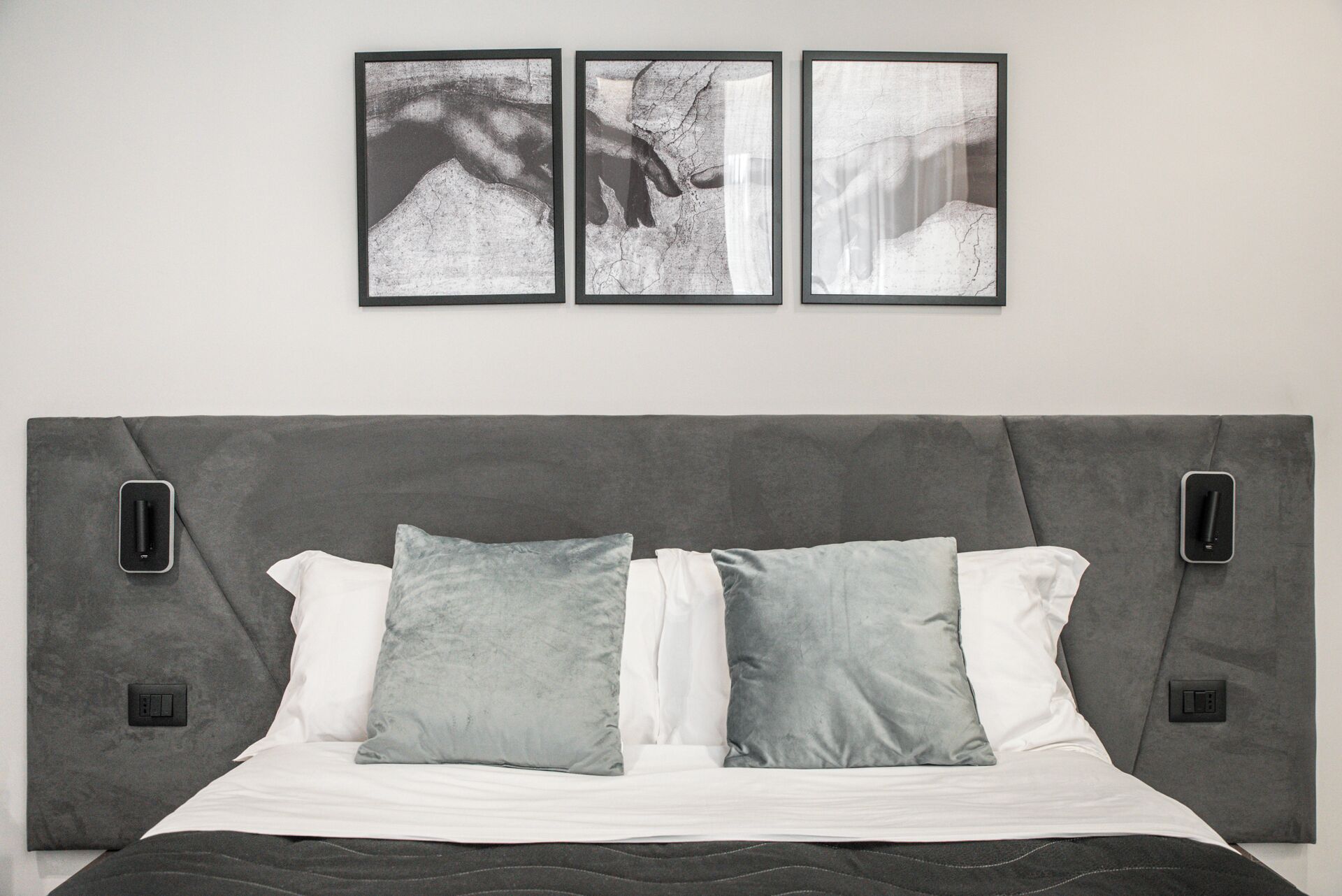 A bedroom with a grey headboard, white and grey pillows, and three black-framed pictures on the wall.