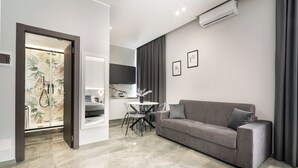 A modern living room with a grey sofa, a dining table with chairs, and a kitchen area in the background. - Karma6Rooms (Catania)