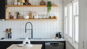 A modern kitchen with white tiled walls, wooden shelves, and a built-in dishwasher. - Burnie Retreat - Coastal Comfort Awaits (Burnie)