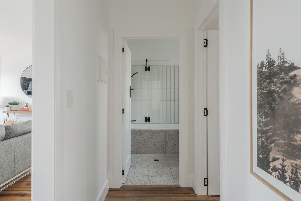 A narrow hallway leading to a bathroom with a shower, tiled walls, and a framed picture on the wall.