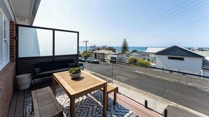 A balcony with a wooden table and seating, overlooking a street and houses. - Burnie Retreat - Coastal Comfort Awaits (Burnie)