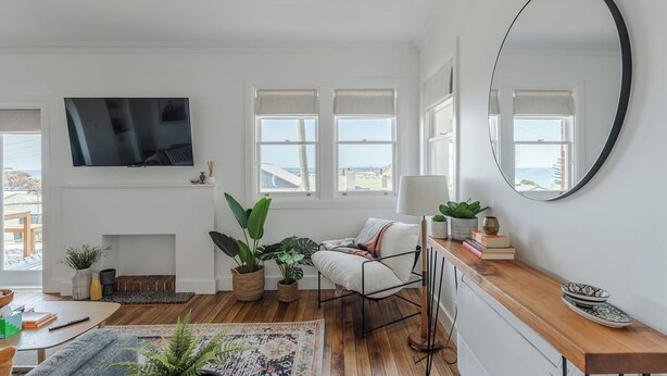 A modern living room with a TV, fireplace, plants, and a large mirror. - Burnie Retreat - Coastal Comfort Awaits (Burnie)