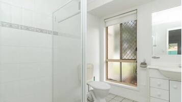 A bathroom with a toilet, a window with a metal screen, and a shower area.