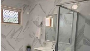 Une salle de bain avec un mur en marbre, une douche en verre, un lavabo et une fenêtre donnant sur un beau paysage.
