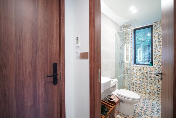 A bathroom with a wooden door, a toilet, a shower, and a window. - The Coral Homestay & Pub (Da Nang)